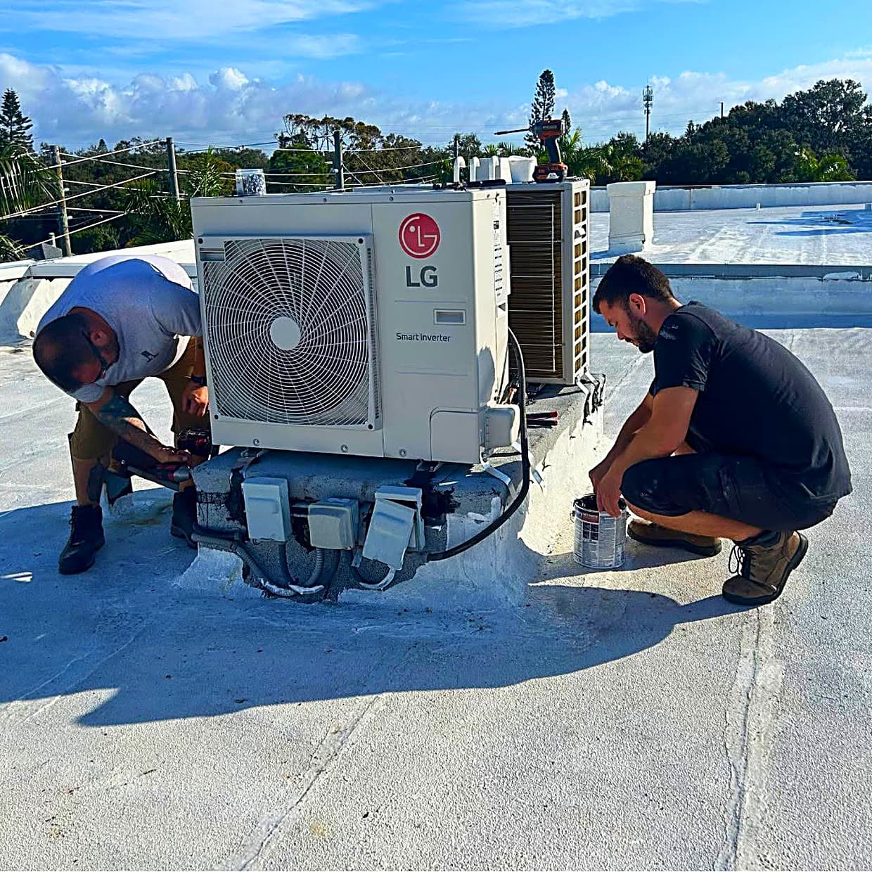 Two J&J technicians servicing a condensing unit on a flat commercial roof