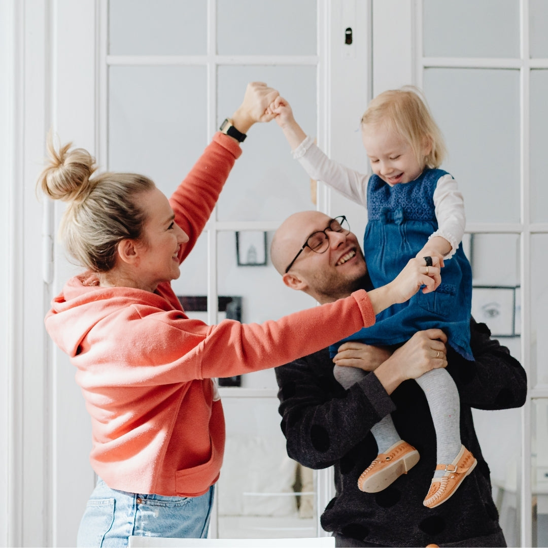 Family of three, are dancing together in a home setting.